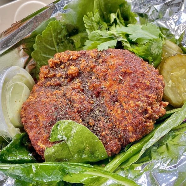 Taiwanese fried chicken cutlet with herbs, fresh greens, pickles, and a side of sauce in foil.