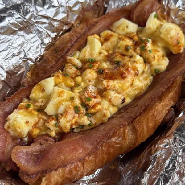 Taiwanese-style bacon-wrapped hot dog topped with scrambled eggs and chives, served in foil.