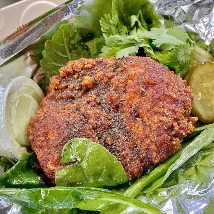 Crispy Taiwanese fried chicken cutlet with herbs, fresh greens, pickles, and a side of sauce in foil.