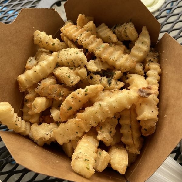 Close-up of golden, seasoned crinkle-cut fries in a brown paper container from Java Saga.