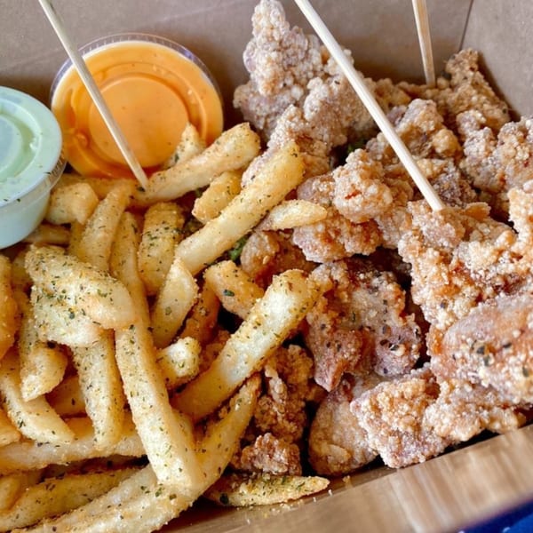 Taiwanese popcorn chicken and seasoned fries with two dipping sauces in a cardboard box.