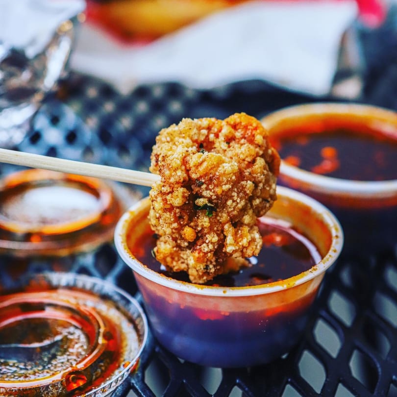 Crispy Taiwanese popcorn chicken on a skewer, dipped into a small cup of dark sauce.